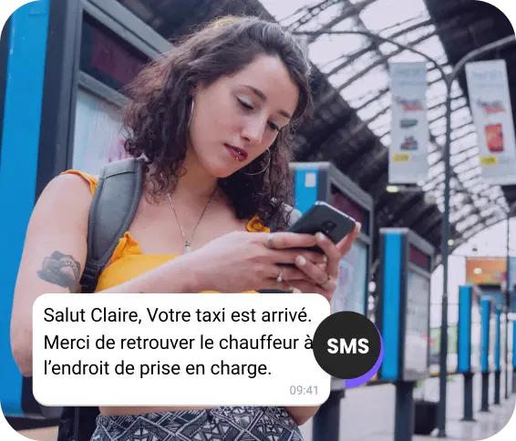 Une jeune femme avec un sac à dos attend à la station et lit un SMS concernant l'arrivée de son taxi.
