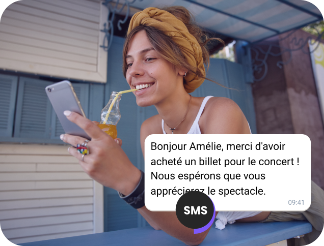 Une jeune femme dégustant un jus en pleine rue consulte un SMS de confirmation pour son billet de concert dans une campagne marketing.
